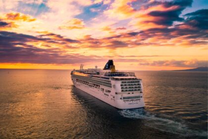 Cruise ship sailing across the ocean under a vivid sunset sky