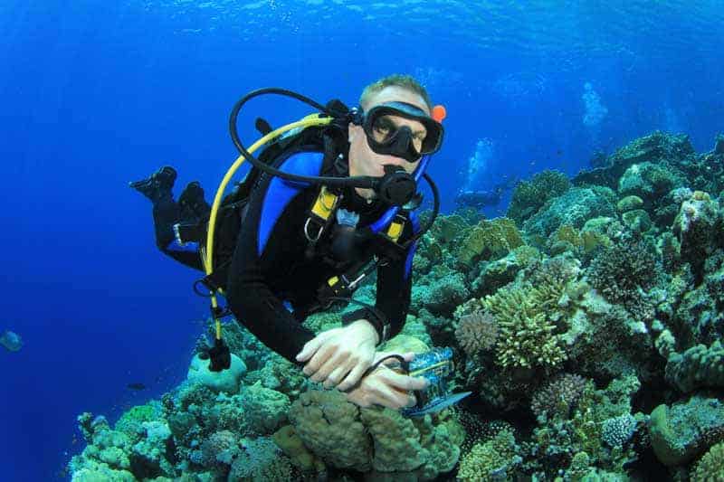 Diver hovering in neutral buoyancy above a coral reef while holding a camera
