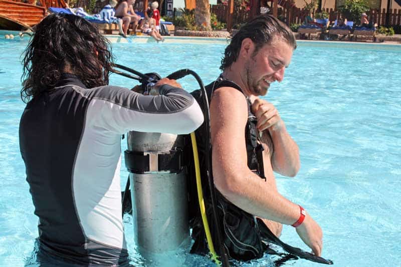 Dive instructor helping a student put on scuba gear during a pool lesson
