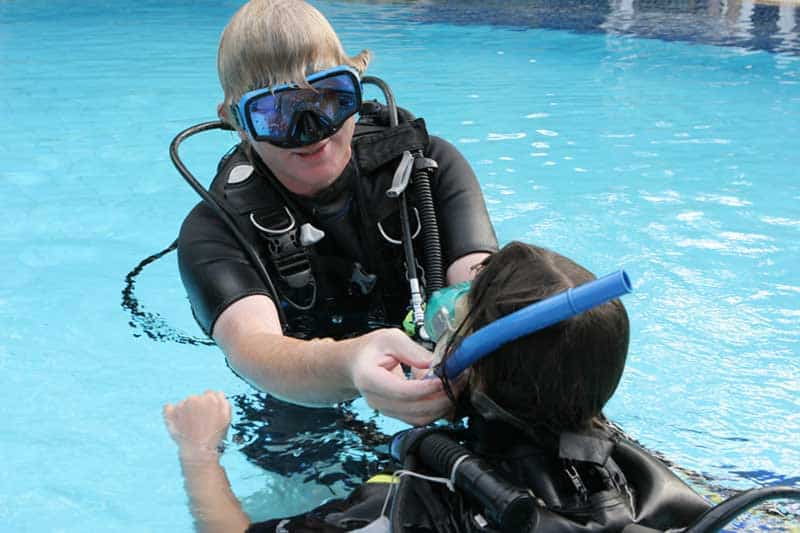 Instructor Assisting Young Diver Dive instructor helping a young student position their regulator mouthpiece in a swimming pool