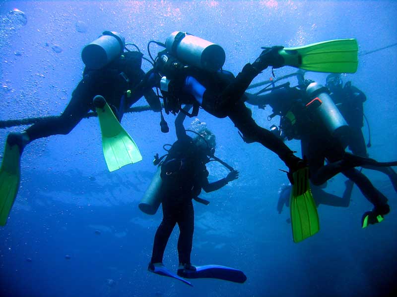 Divers Holding Anchor Line Group of scuba divers holding onto an anchor line underwater, fins spread out during a training dive
