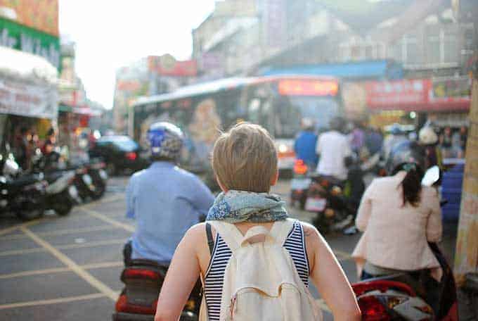 Backpacker walking through a crowded street market busy with mopeds and traffic
