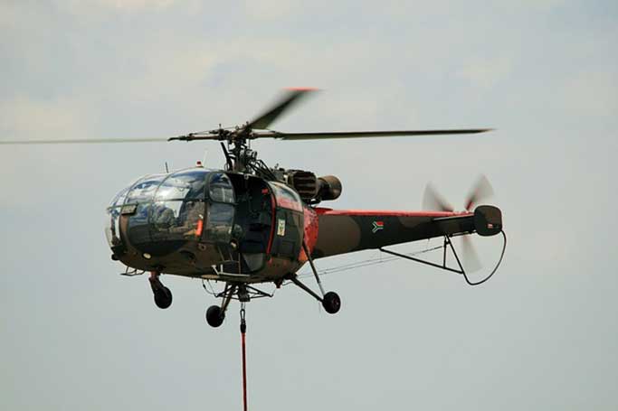Camouflage rescue helicopter marked with a South African flag flying under clouds