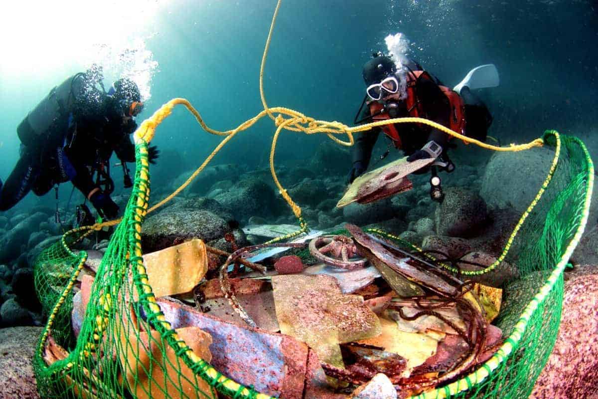 Two divers hauling a net full of collected trash and debris up from a rocky seafloor
