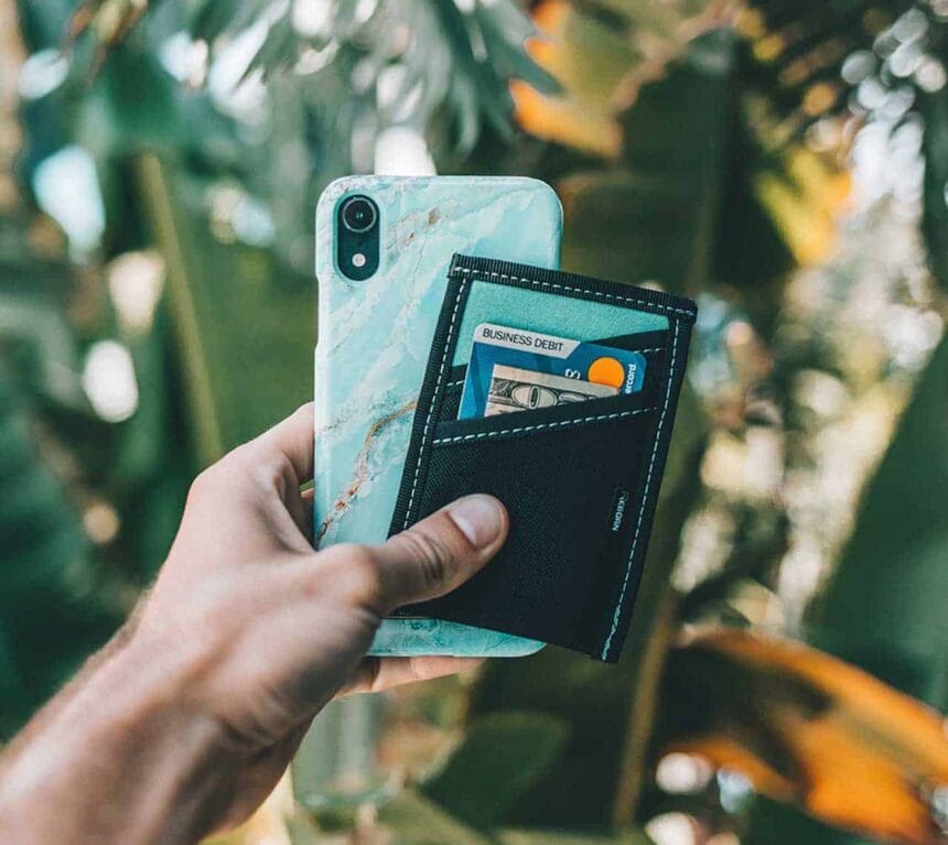 Reborn Rubber Wallet In Jungle Reborn Rubber wallet attached to a phone case, held up amid tropical foliage