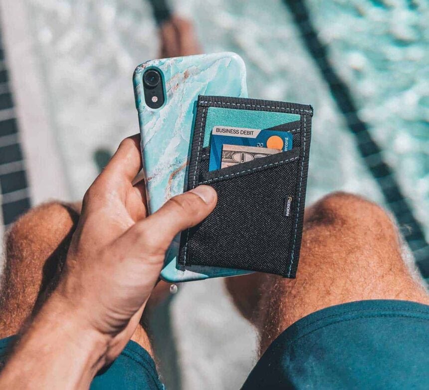 Reborn Rubber Wallet Poolside Reborn Rubber wallet attached to a phone case, held poolside with a debit card and cash visible