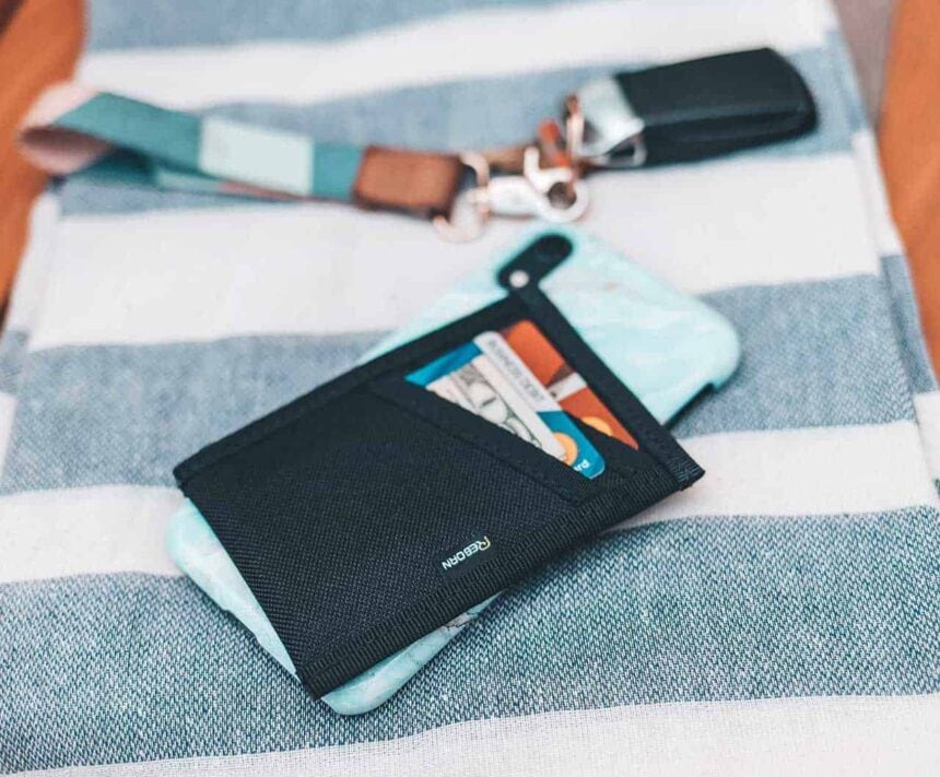 Reborn Rubber Wallet And Wristlet Reborn Rubber wallet resting on a striped towel next to a phone and wristlet keychain