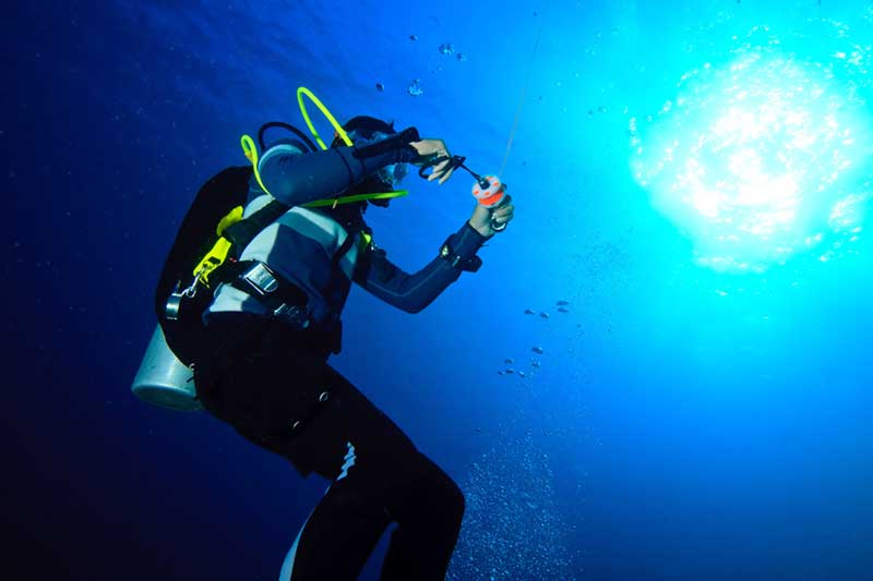 Diver spooling out line from a reel while sending up a marker buoy