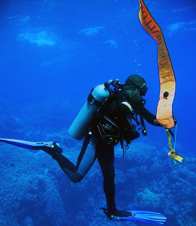 Diver hovering by a reef with an inflated orange DSMB marker buoy