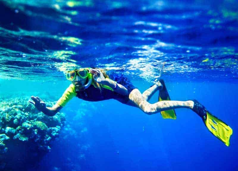 Young snorkeler in mask and yellow fins gliding along a shallow reef edge