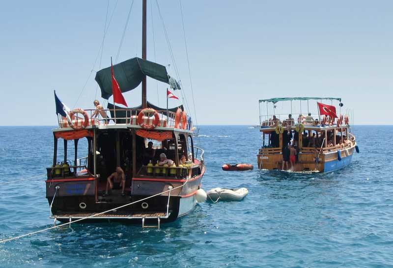 Two wooden dive boats anchored off the Turkish coast, one flying the Turkish flag