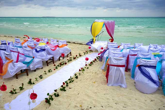 Rows of draped white chairs and a rose petal aisle lead to a canopy on the beach for a second ceremony