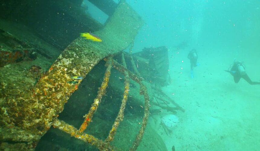 Encrusted frames of the Star Gerren wreck in Aruba with two scuba divers hovering over the sand behind