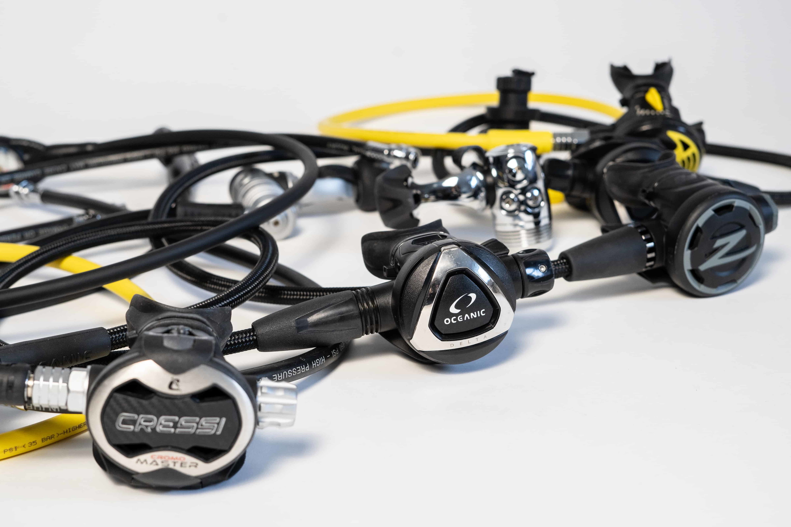 regulators from Cressi, Oceanic and another brand displayed together with hoses