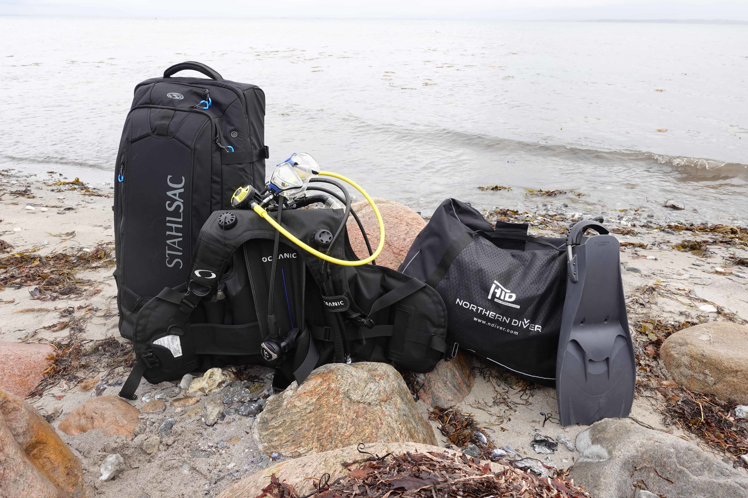 Stahlsac roller bag, Northern Diver dry duffel, BCD and fins staged on a rocky beach for DIVEIN dive bag testing