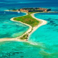 Aerial view of a small Florida island with a historic brick fort, a curving sandbar and turquoise shallows