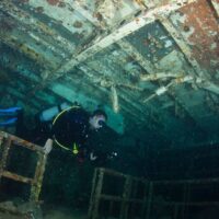 Scuba diver with a torch swimming inside the hull of a large shipwreck
