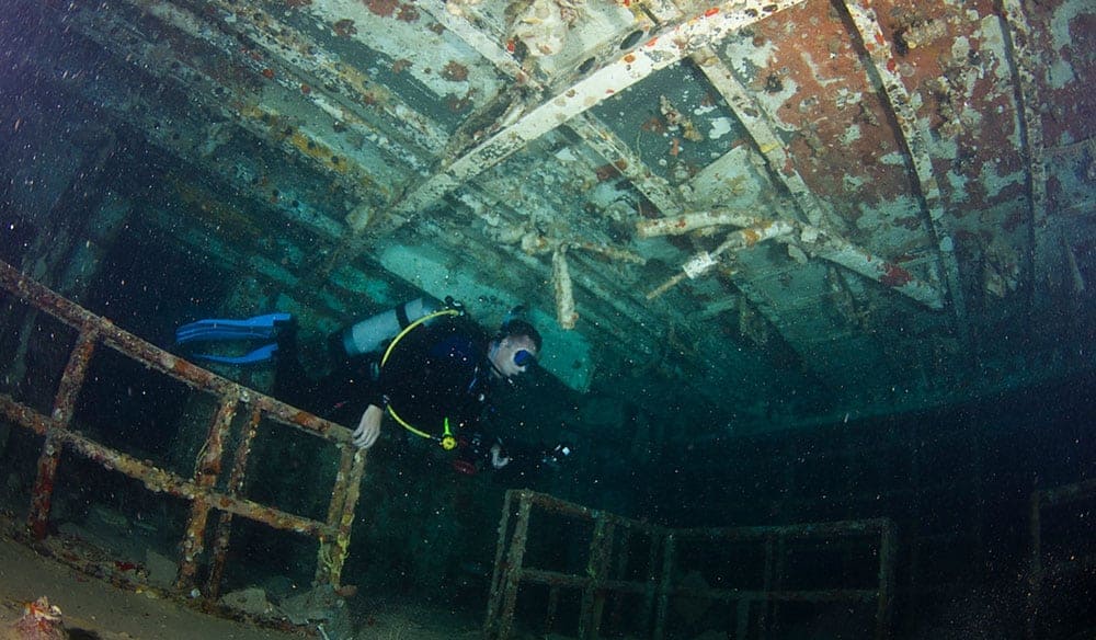 Scuba diver with a torch swimming inside the hull of a large shipwreck