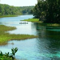 Canoeists paddling the clear turquoise water of Florida's Rainbow River between grassy banks and forest