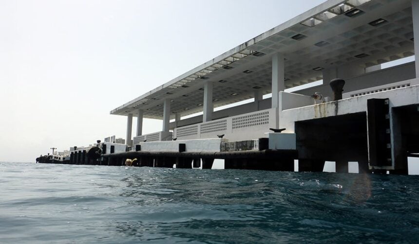 Long concrete pier stretching out over the sea photographed from the waterline with a diver alongside