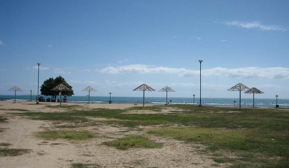 Sandy shoreline park with metal shade shelters and light surf under a bright blue sky
