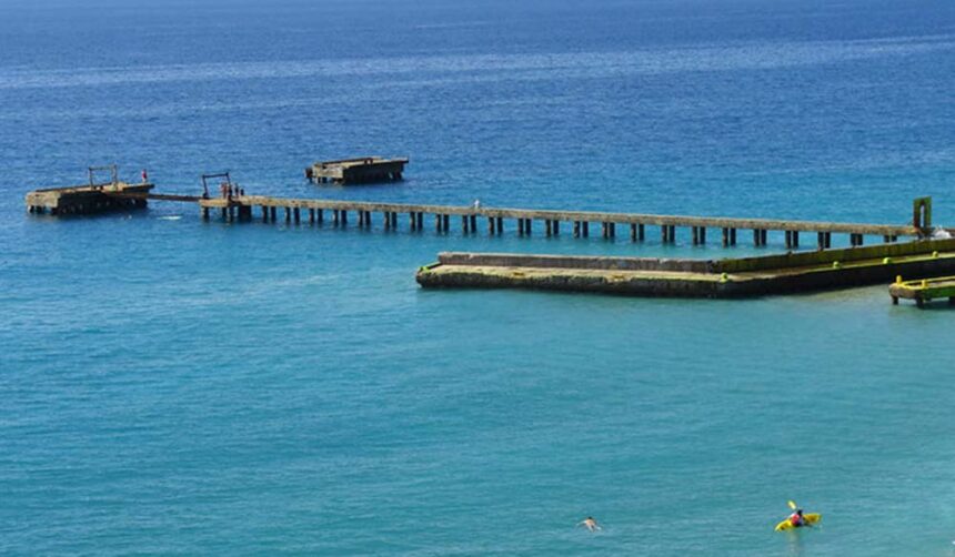 Long wooden pier reaching out over turquoise water with swimmers and a yellow kayak nearby