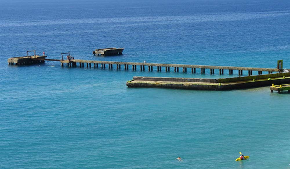 Long wooden pier reaching out over turquoise water with swimmers and a yellow kayak nearby