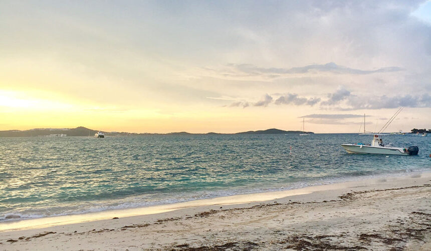 Sunset over a calm bay with a white centre console boat anchored off a sandy beach