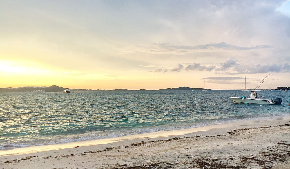 Sunset over a calm bay with a white centre console boat anchored off a sandy beach