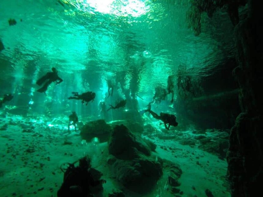 divers descending into a sunlit cenote cavern in Mexico, silhouetted against beams of light