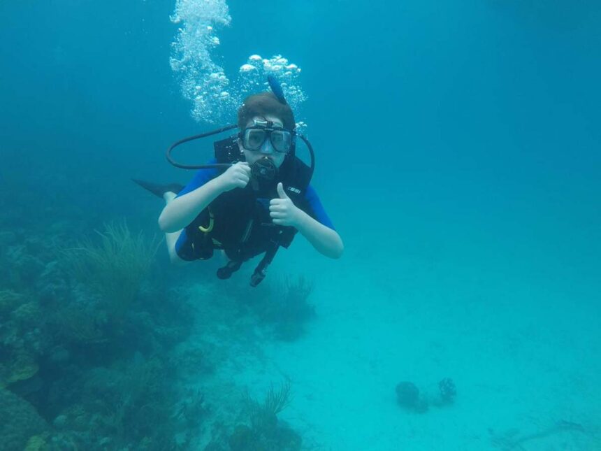 Young diver giving a thumbs up underwater near a coral reef