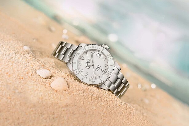 Davosa Ternos Medium dive watch with white dial resting in beach sand beside seashells