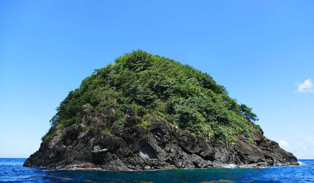 Rocher de la Perle rising as a steep green rock islet from deep blue sea off Martinique