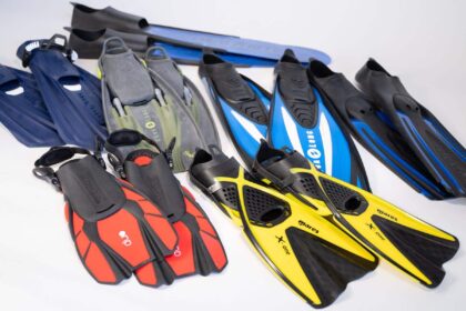 an assortment of snorkeling fins in navy, olive, blue, red and yellow laid out on white