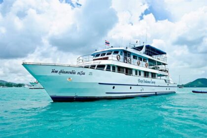 the multi-deck liveaboard Deep Andaman Queen anchored in turquoise water with a Thai flag at the stern