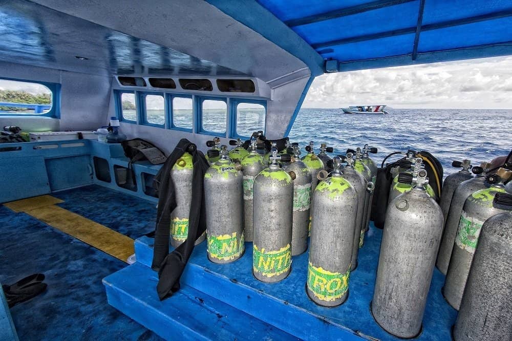 Rows of scuba tanks labeled Nitrox lined up on a dive boat with the ocean in the background