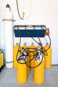 Yellow scuba tanks connected by hoses to a nitrox gas blending and filling station