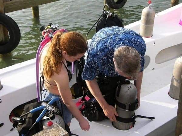 two divers gearing up with tanks and equipment on a dive boat deck