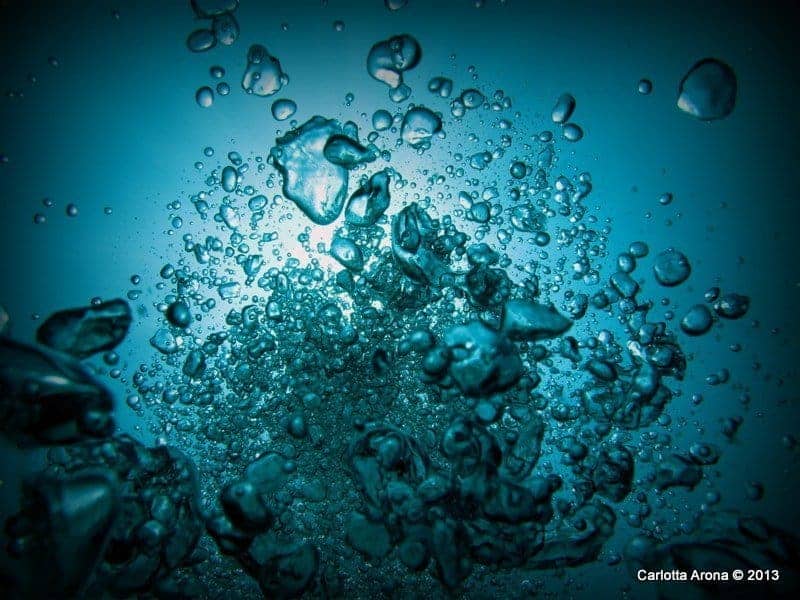 A diver's exhaled bubbles rising through glowing blue water