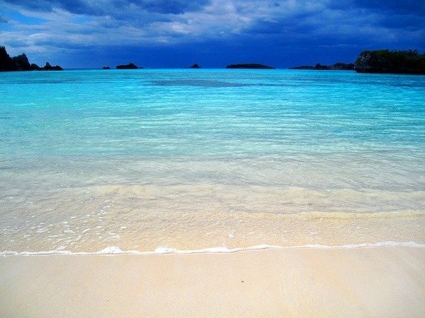 Turquoise shallows meet white sand under stormy skies at a tropical dive destination