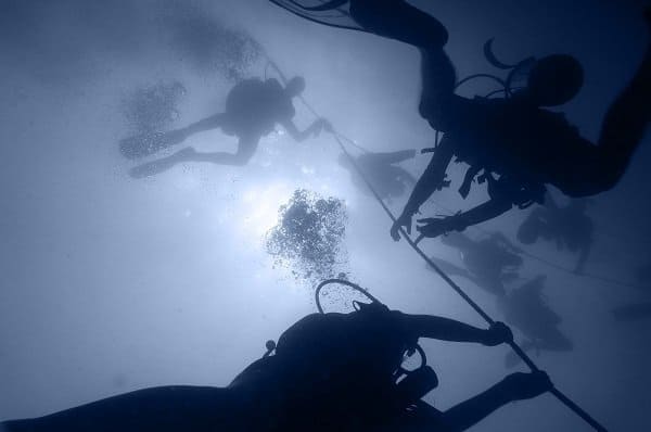 Divers hold onto a line during a safety stop with bubbles rising toward the surface