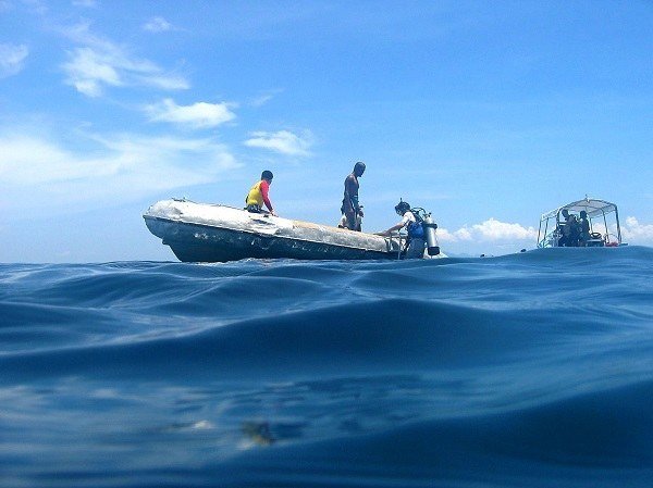 Divers gear up on a small inflatable boat with a larger dive boat anchored nearby