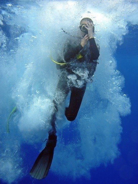 A diver descends through a cloud of bubbles just after entering the water