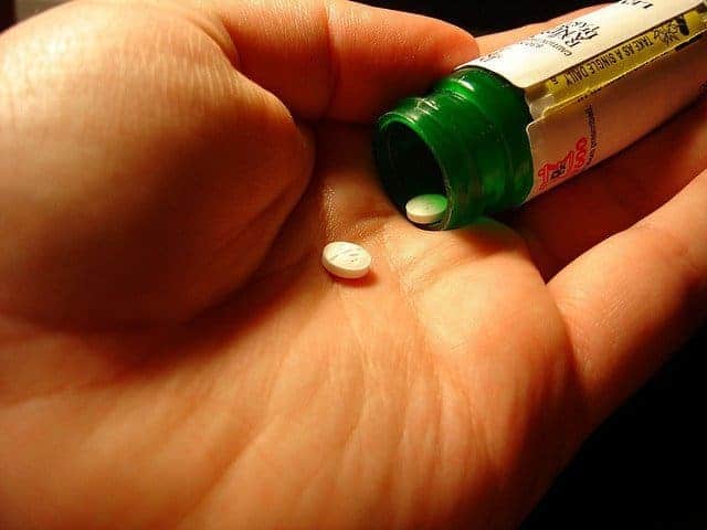 Hand holding a motion sickness tablet next to its opened pill bottle