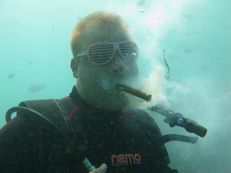 Diver underwater with a cigar in his mouth blowing a smoky cloud