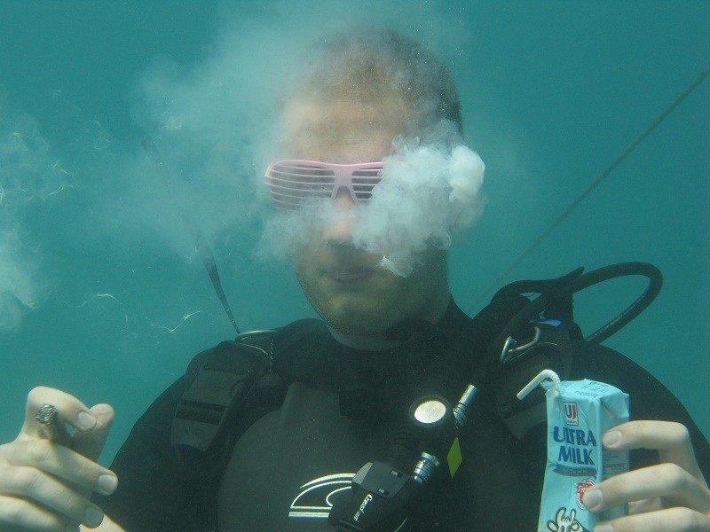 Diver in shutter shades blows a smoky milk cloud while holding a milk carton underwater