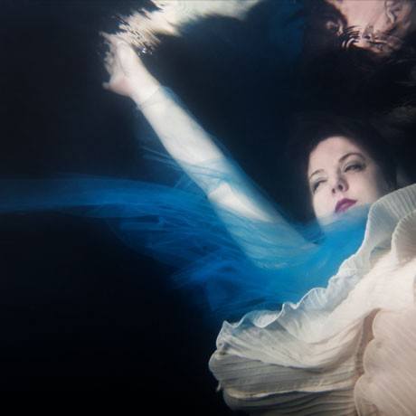 Underwater portrait of a cancer survivor in a flowing white dress against dark water