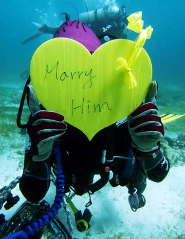 Diver holding up a yellow heart sign asking marry him underwater