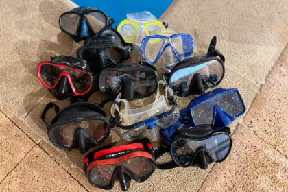 Pile of eleven dive and snorkel masks laid out on a tiled pool deck after testing