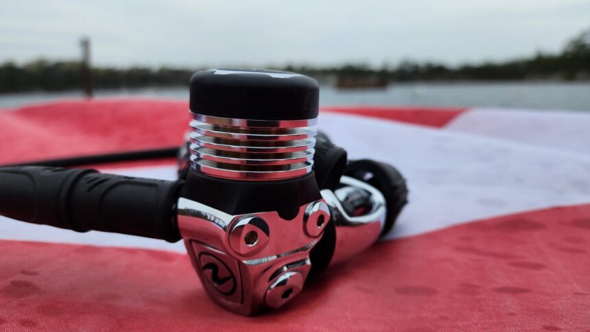 Chrome Aqualung Leg3nd Elite first stage resting on a red and white cloth at the water's edge